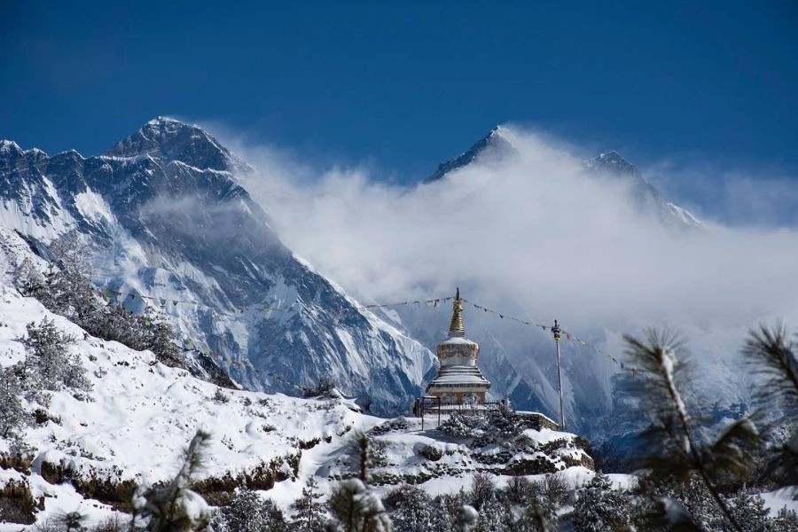 Snow-covered stupa with Himalayan peaks in the background.